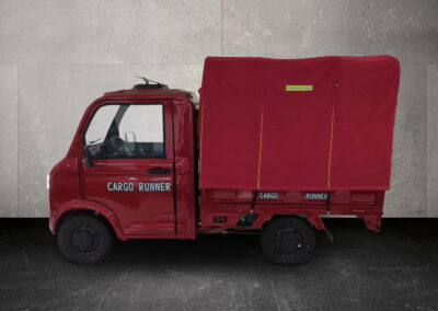 Seitenansicht des Cargo Runner Toro in Rot mit Kipppritsche auf grauem Hintergrund